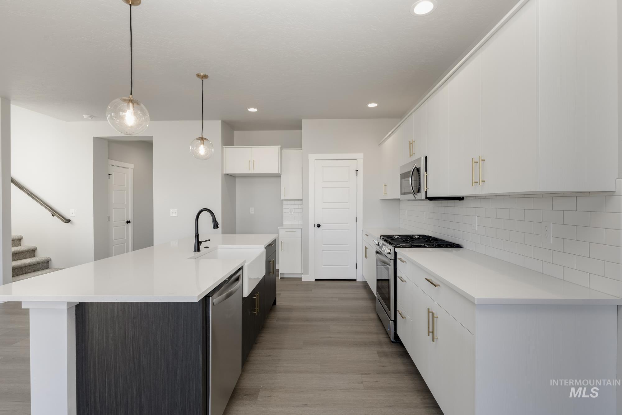 Kitchen featuring white cabinets, appliances with stainless steel finishes, backsplash, a kitchen island with sink, and light wood-type flooring