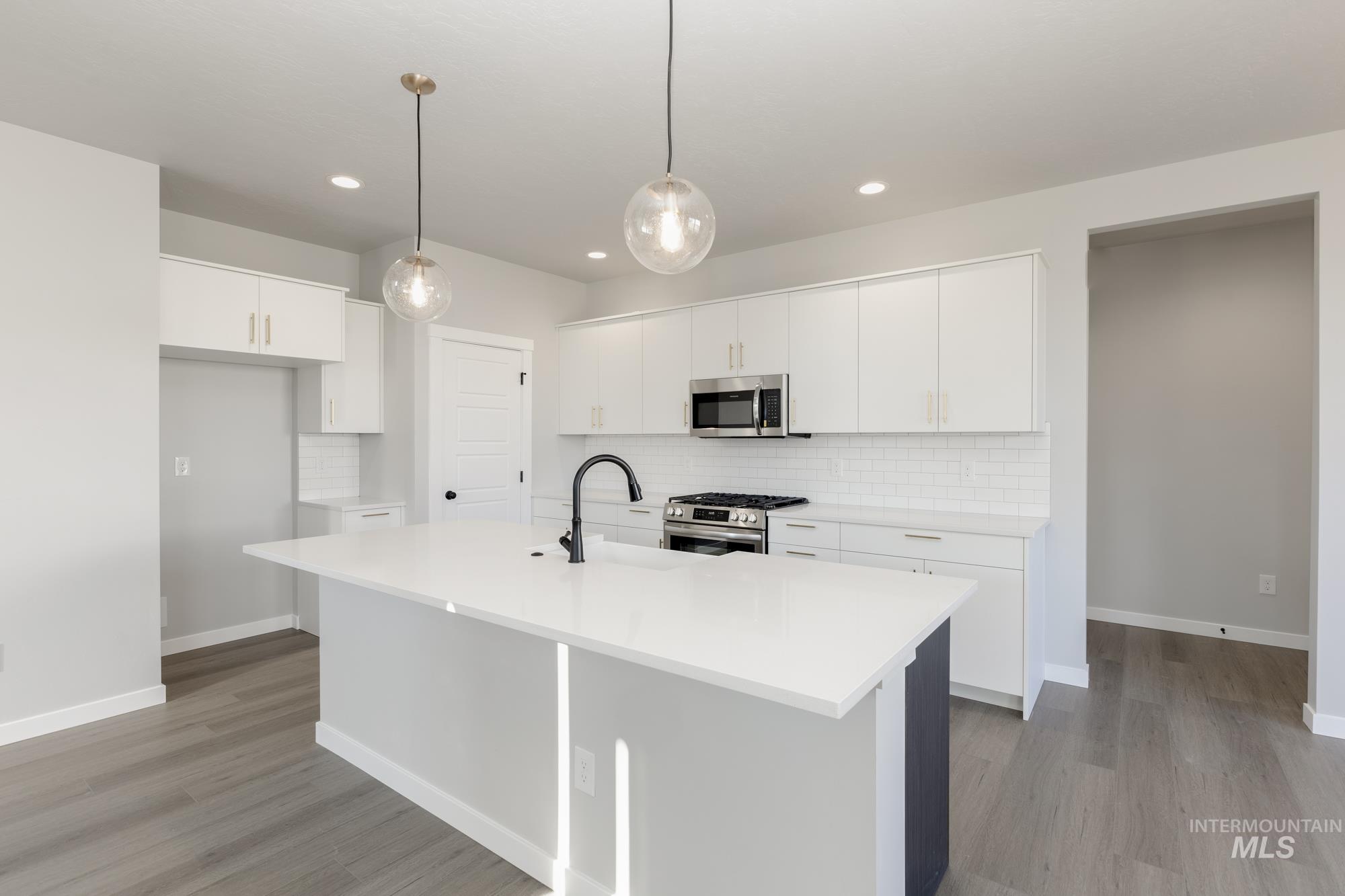 Kitchen with an island with sink, backsplash, appliances with stainless steel finishes, hanging light fixtures, and white cabinetry