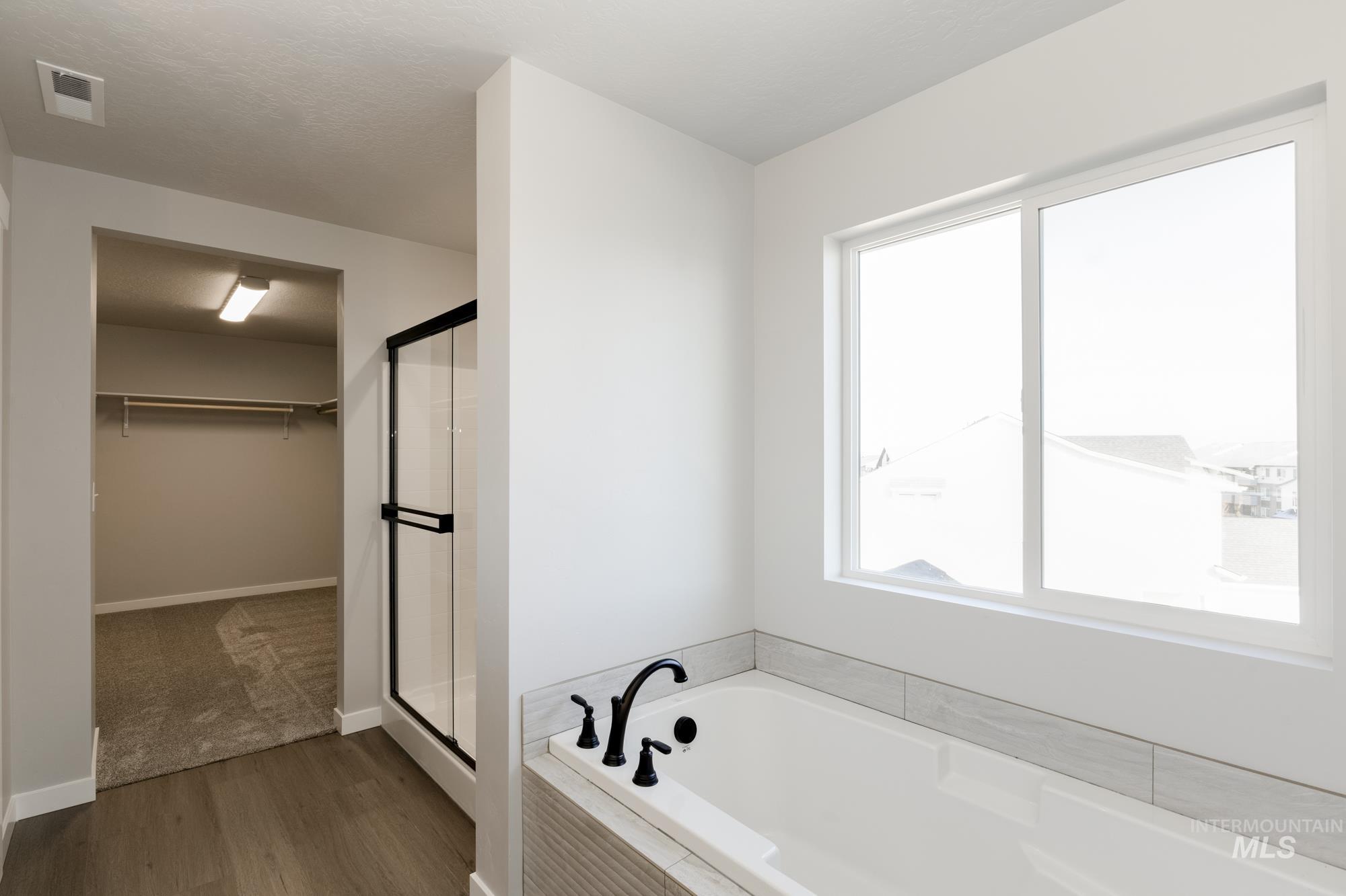 Full bath with plenty of natural light, a bath, a spacious closet, and dark wood-type flooring