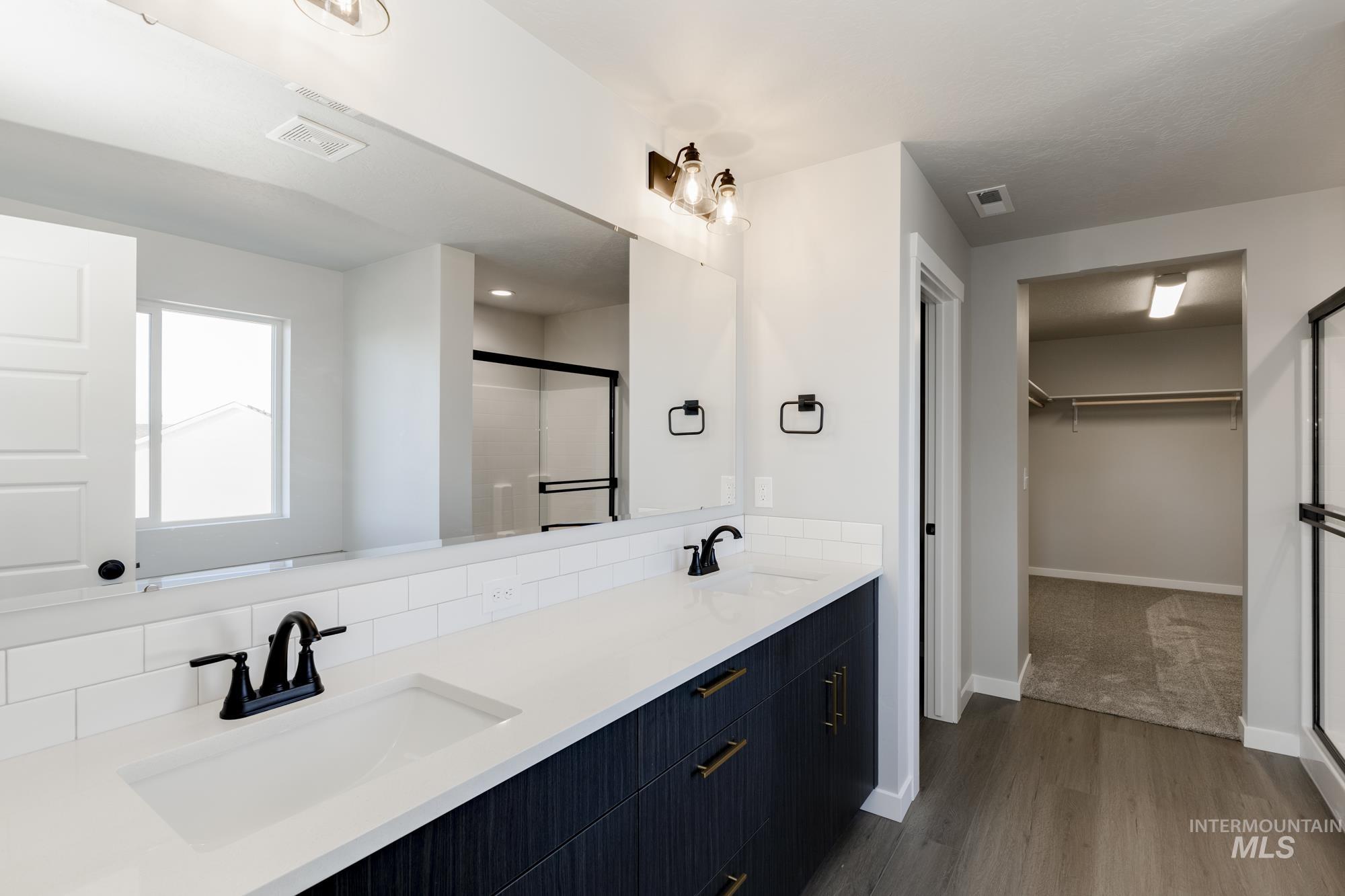 Full bath with a shower stall, a spacious closet, double vanity, and dark wood finished floors