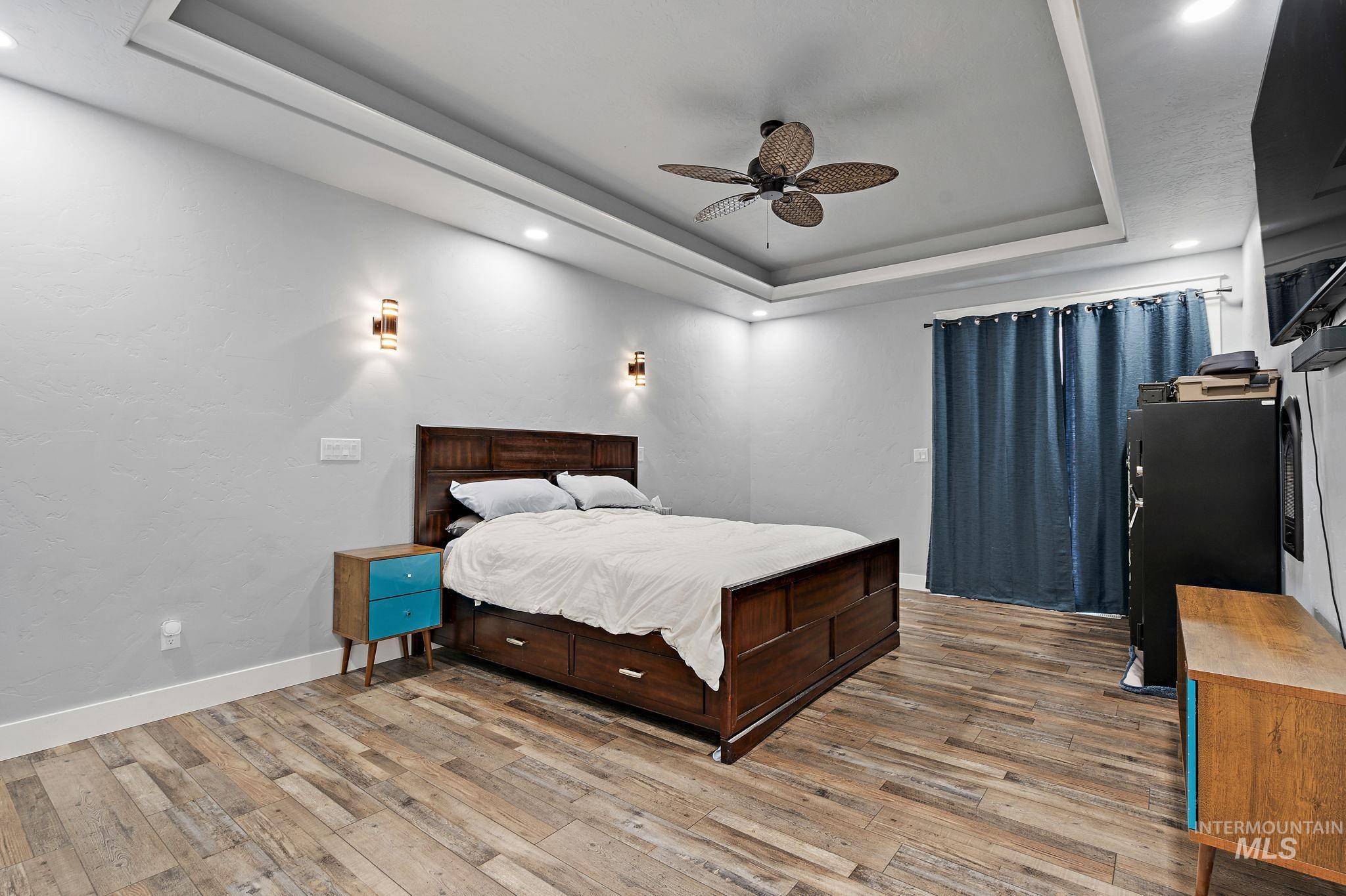 Bedroom with a raised ceiling, light wood-style flooring, ceiling fan, and recessed lighting