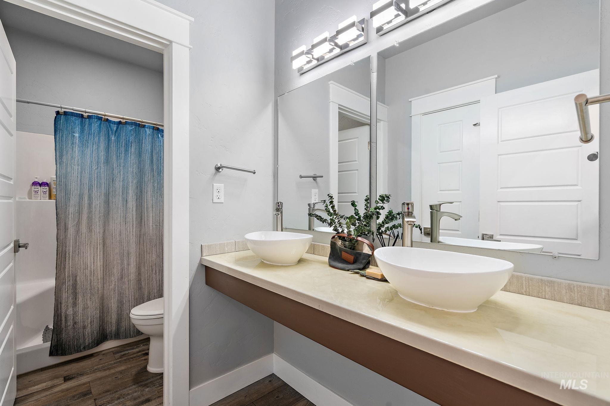 Bathroom featuring dark wood-style flooring, shower / bath combo, and double vanity