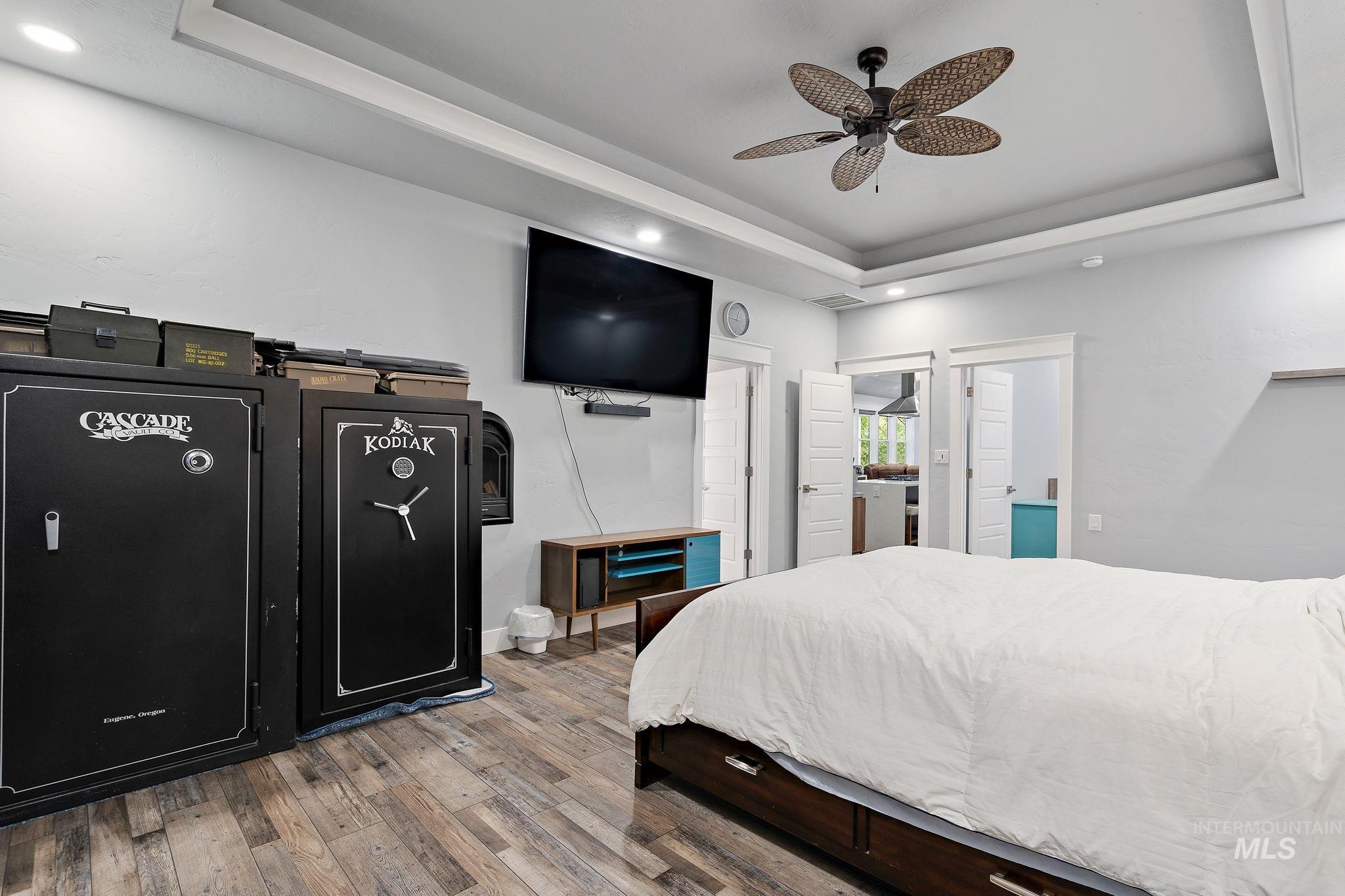 Bedroom featuring a tray ceiling, light wood-type flooring, ceiling fan, recessed lighting, and ensuite bath