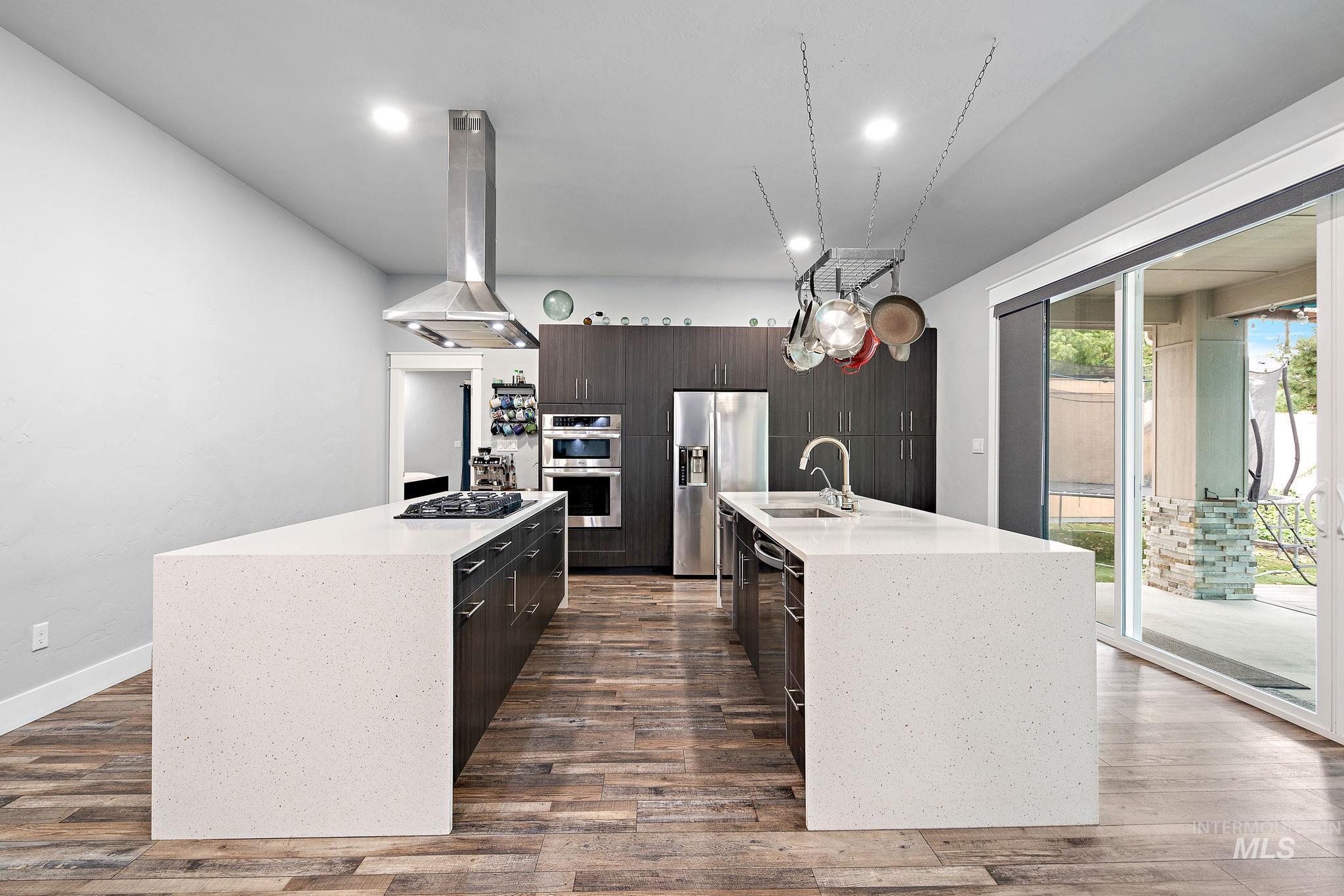 Kitchen with light stone counters, island range hood, dark brown cabinets, stainless steel appliances, and dark wood-style flooring