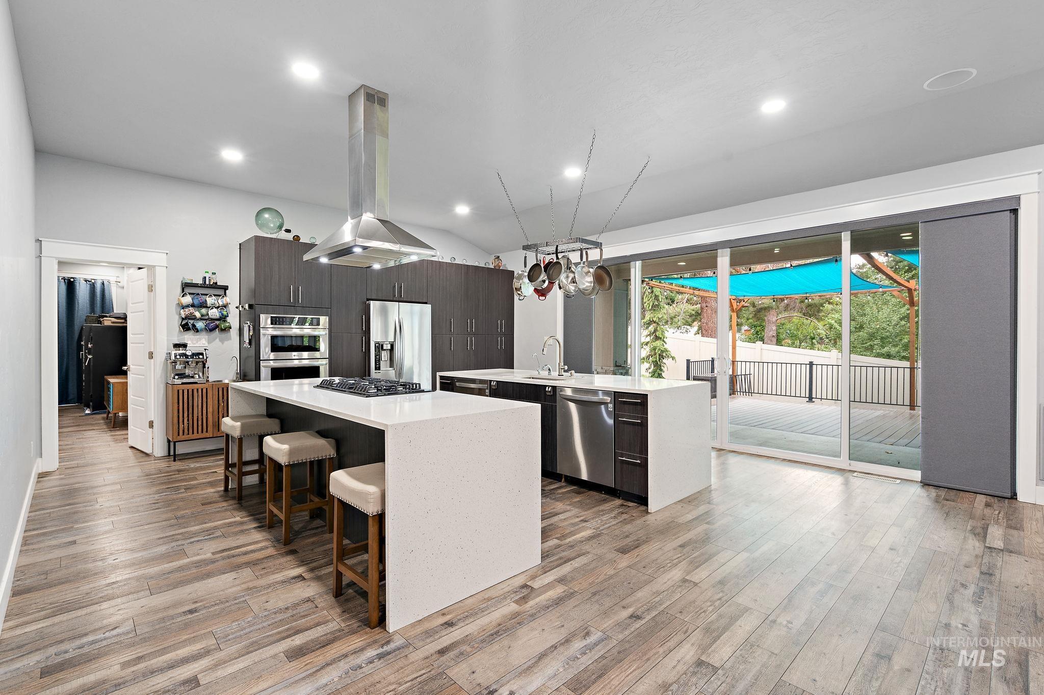Kitchen with modern cabinets, island range hood, light stone countertops, stainless steel appliances, and a breakfast bar