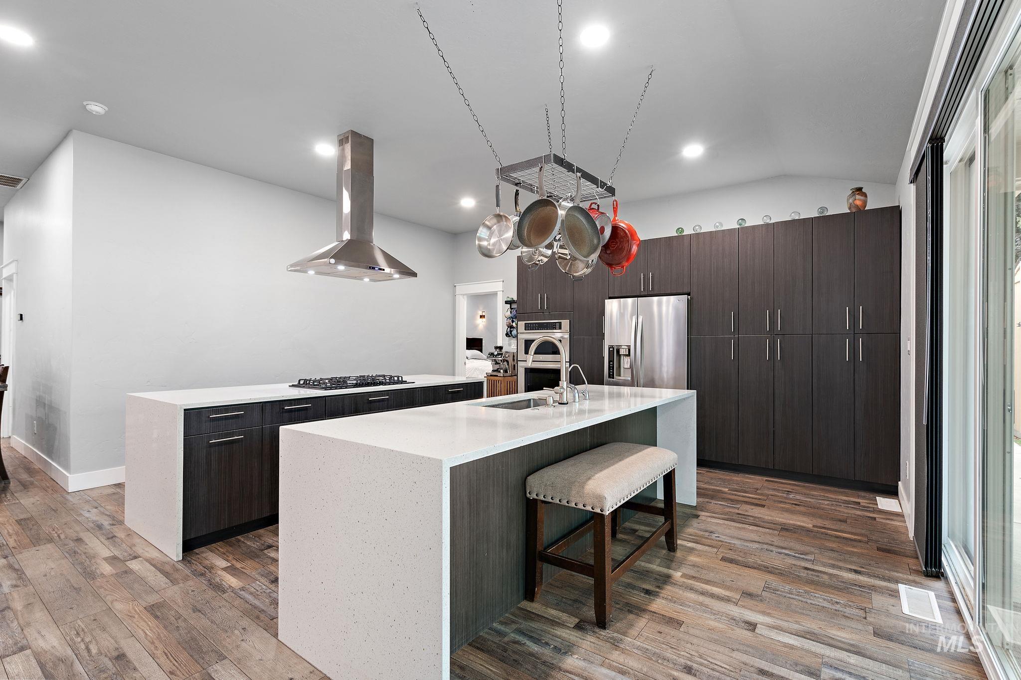 Kitchen with a kitchen breakfast bar, a kitchen island with sink, light wood-style flooring, island exhaust hood, and vaulted ceiling