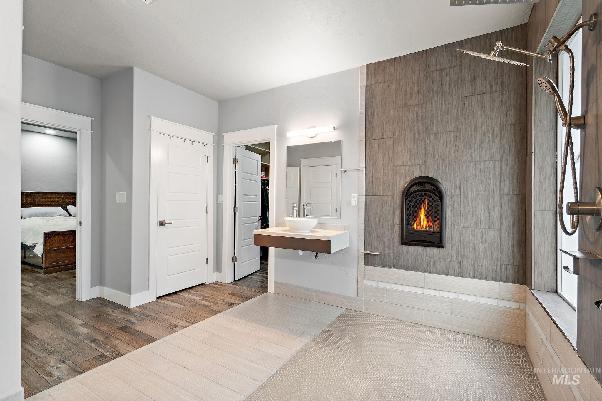 Ensuite bathroom with walk in shower, a fireplace, vanity, and wood finished floors