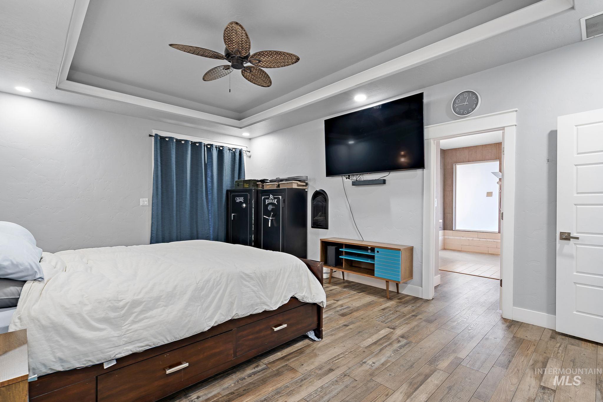Bedroom featuring a raised ceiling, light wood-style floors, and a ceiling fan