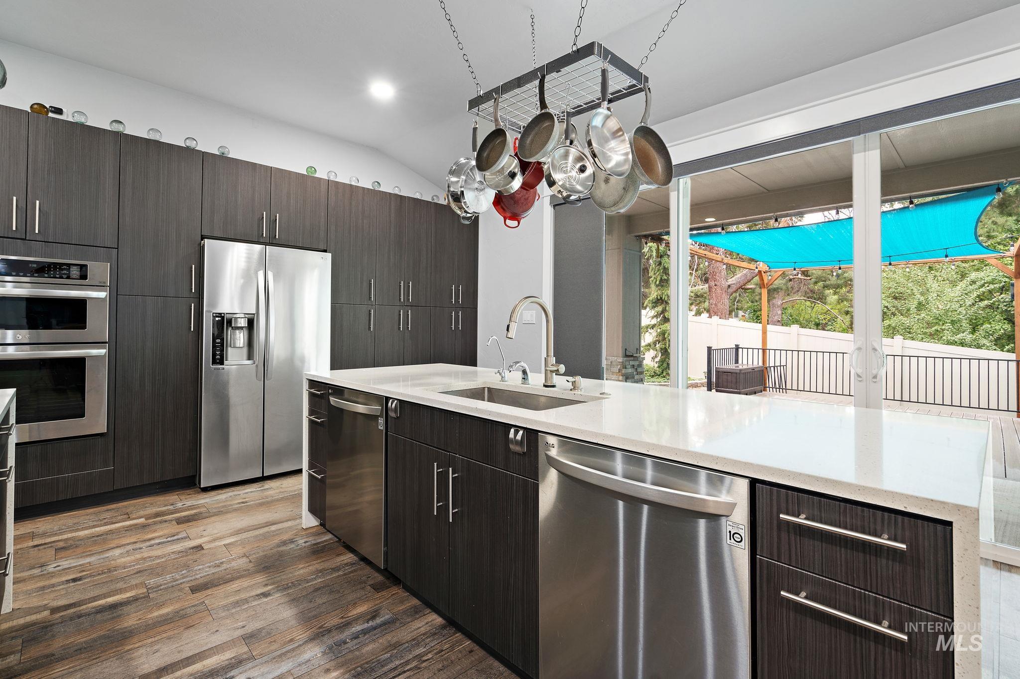 Kitchen with stainless steel appliances, dark brown cabinetry, light stone counters, modern cabinets, and lofted ceiling