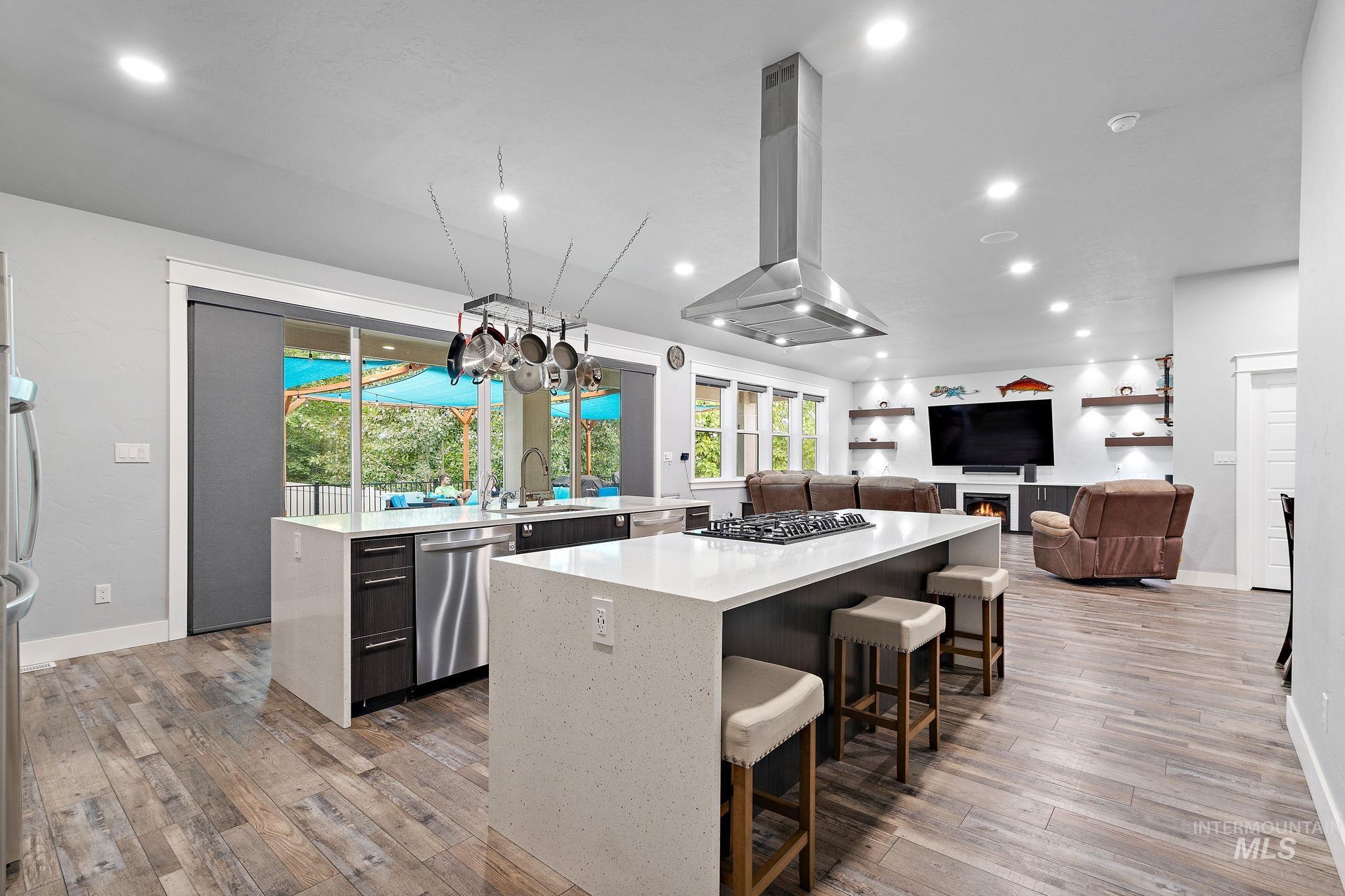 Kitchen featuring light stone counters, range hood, a breakfast bar area, open floor plan, and dishwasher