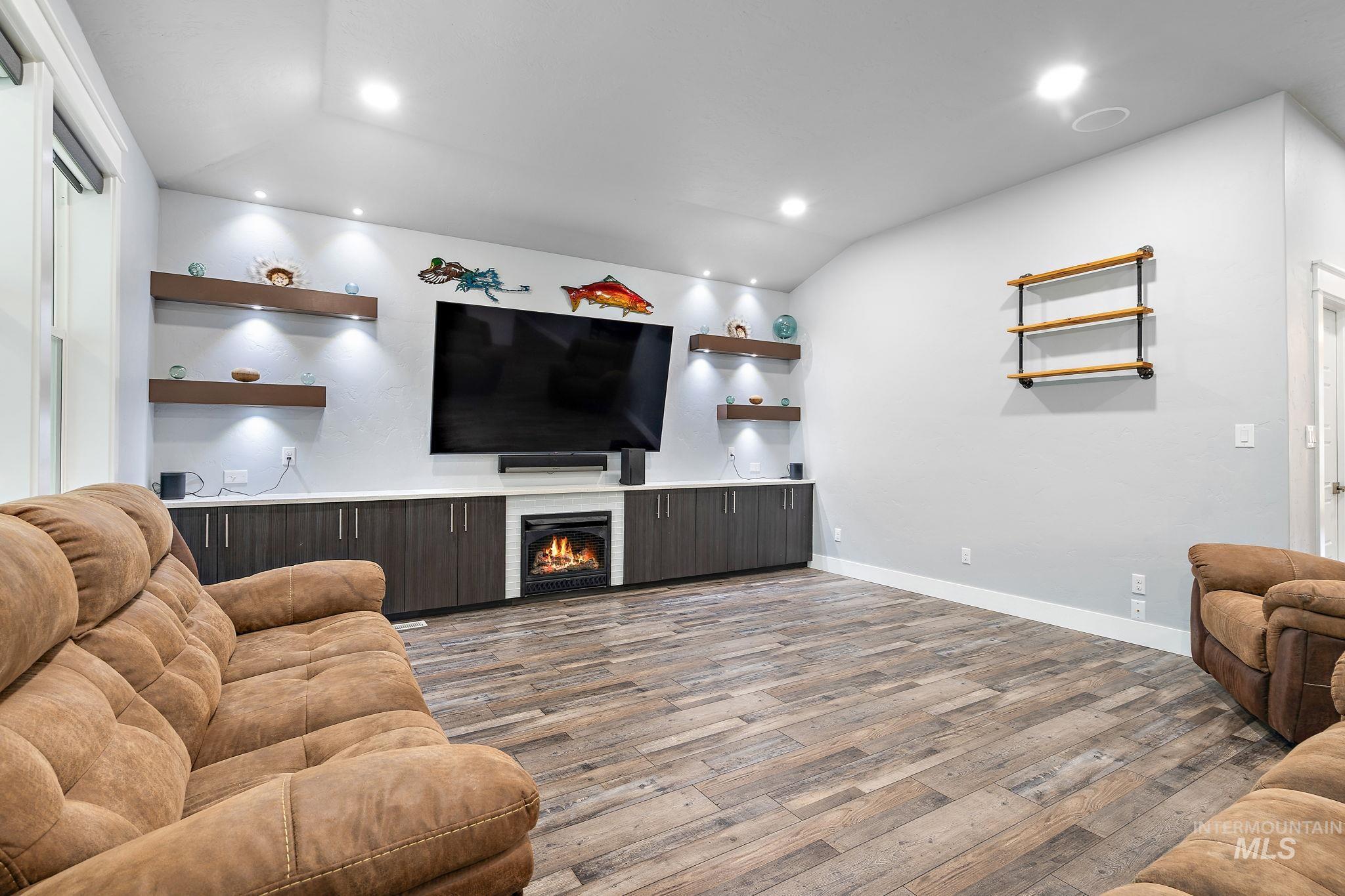 Living area with light wood-style floors, a glass covered fireplace, recessed lighting, and vaulted ceiling