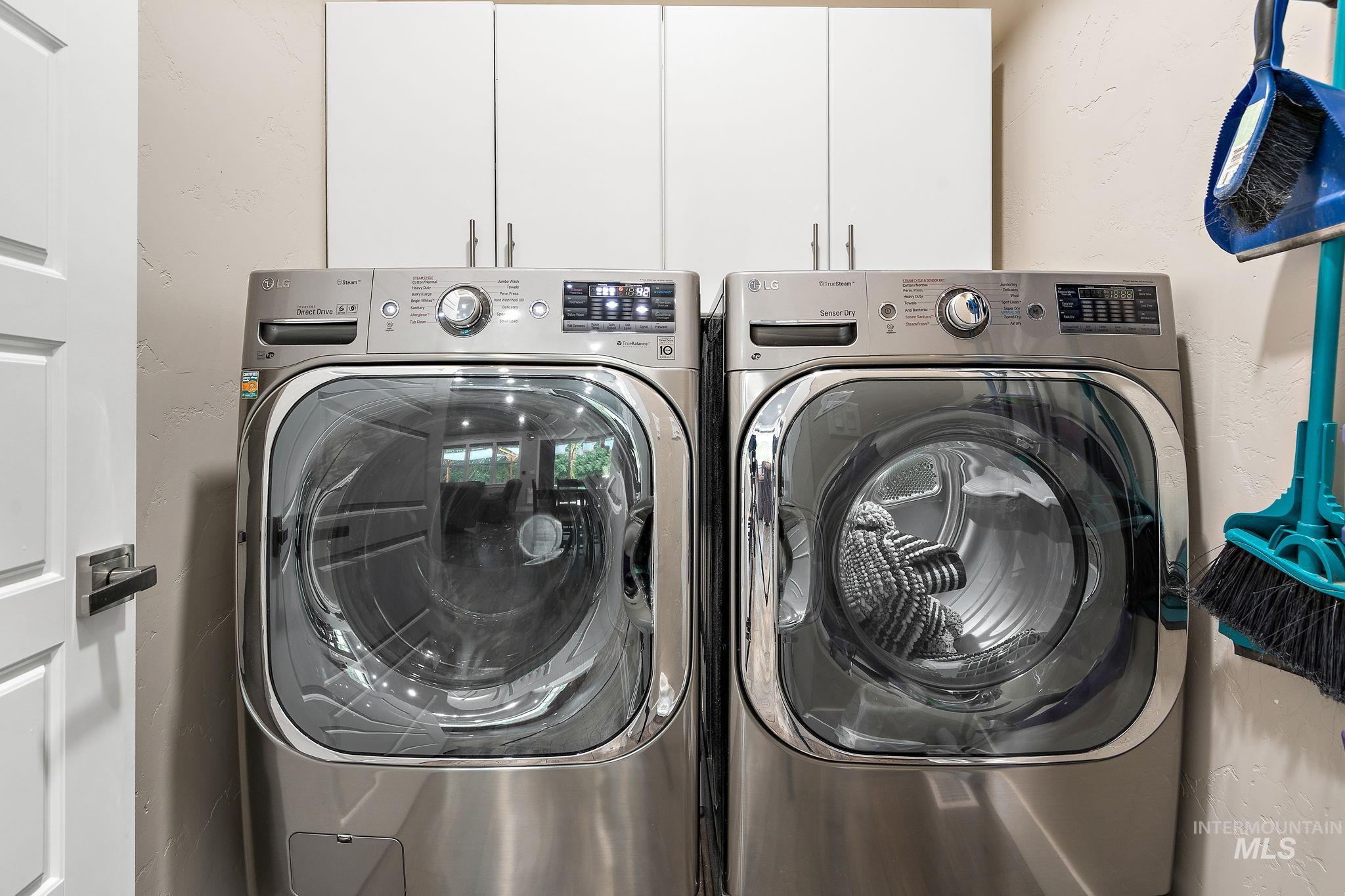 Washroom with a textured wall, washing machine and dryer, and cabinet space