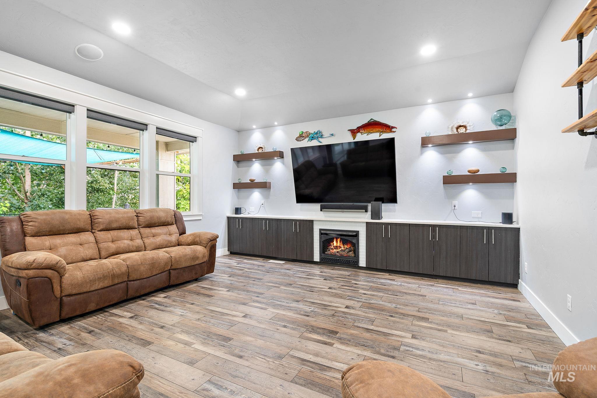 Living room featuring light wood-style flooring, recessed lighting, and a warm lit fireplace