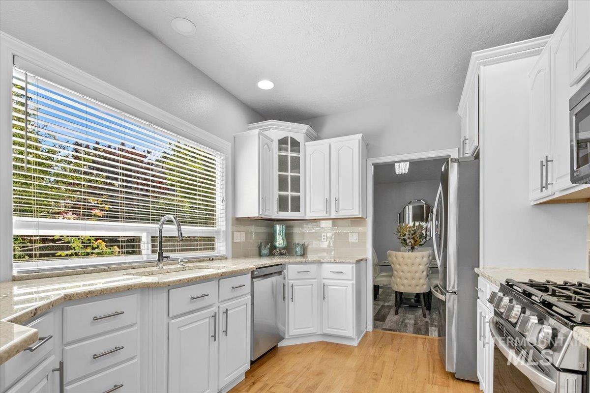 Kitchen featuring glass insert cabinets, light wood finished floors, white cabinets, tasteful backsplash, and recessed lighting