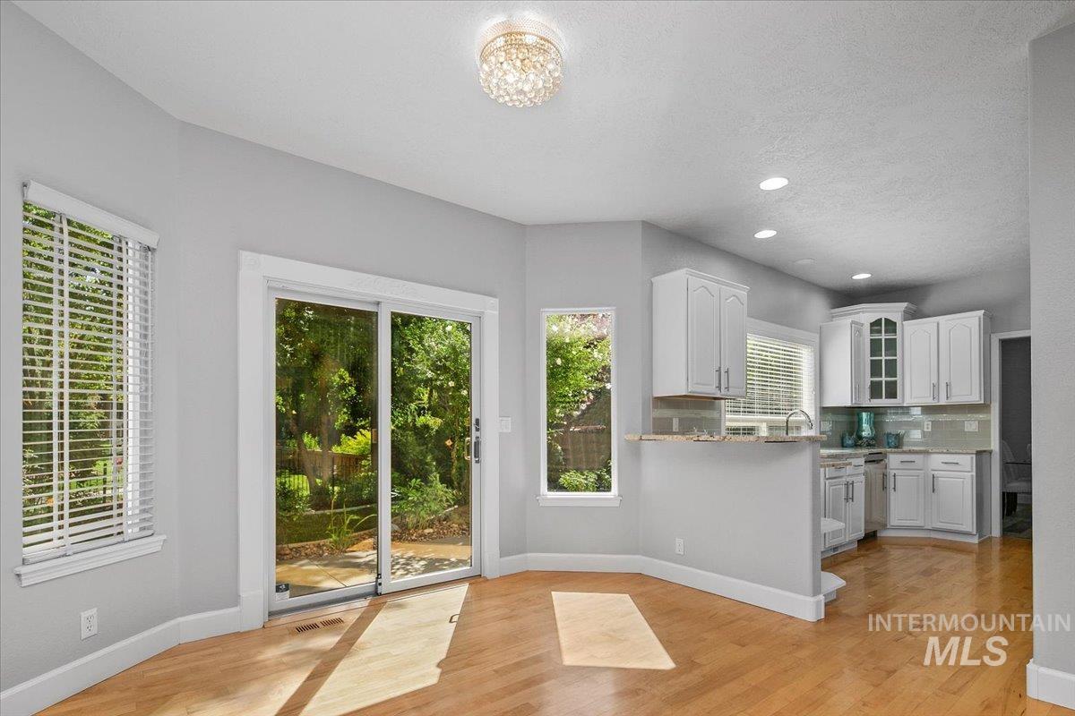 Kitchen with tasteful backsplash, white cabinets, light stone counters, light wood finished floors, and recessed lighting