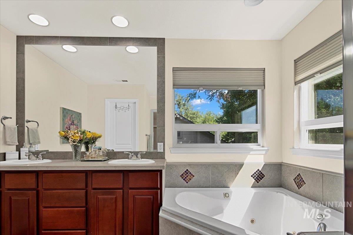 Full bath with double vanity and a tub with jets