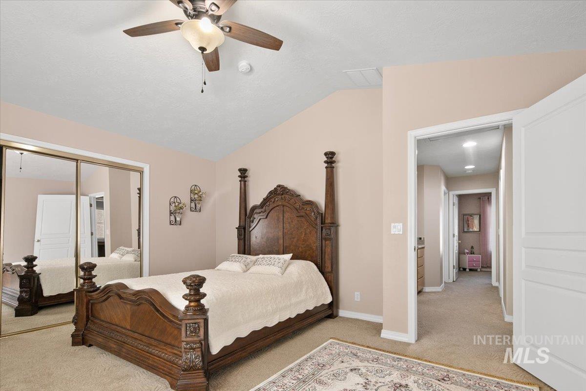 Bedroom with light carpet, a ceiling fan, vaulted ceiling, and a closet