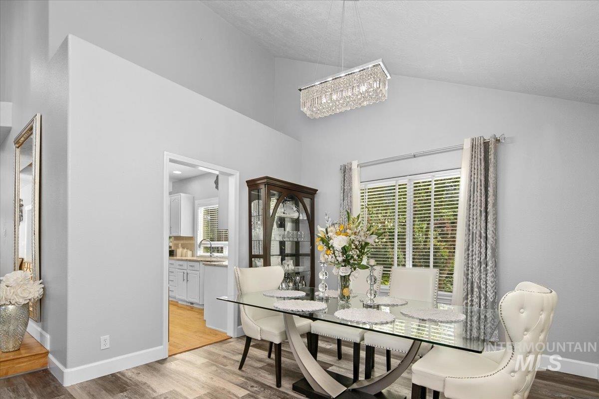 Dining room featuring light wood-style flooring, healthy amount of natural light, a chandelier, and high vaulted ceiling