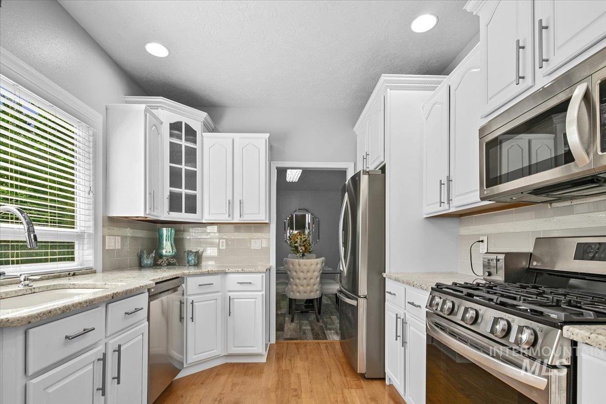 Kitchen featuring appliances with stainless steel finishes, light wood-type flooring, glass insert cabinets, light stone counters, and white cabinets