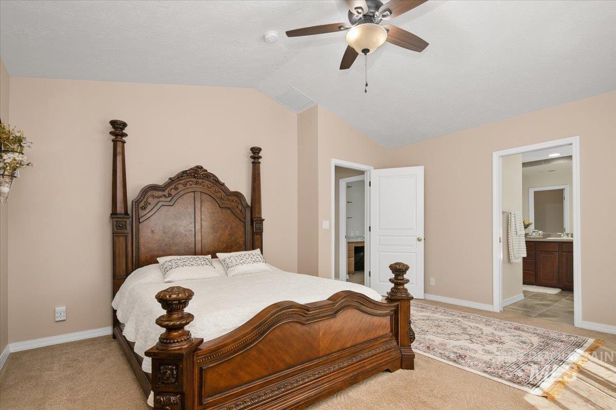 Bedroom with vaulted ceiling, a ceiling fan, light carpet, and connected bathroom