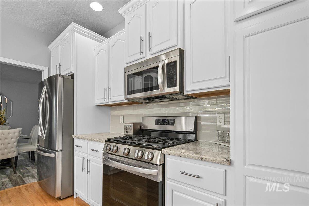 Kitchen featuring stainless steel appliances, backsplash, light wood-style flooring, white cabinets, and light stone counters