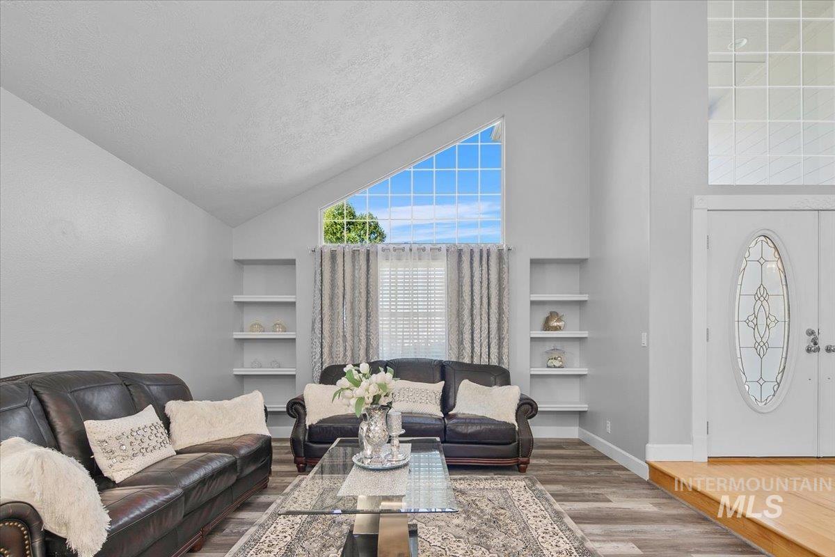 Living room featuring high vaulted ceiling, built in features, wood finished floors, and a textured ceiling