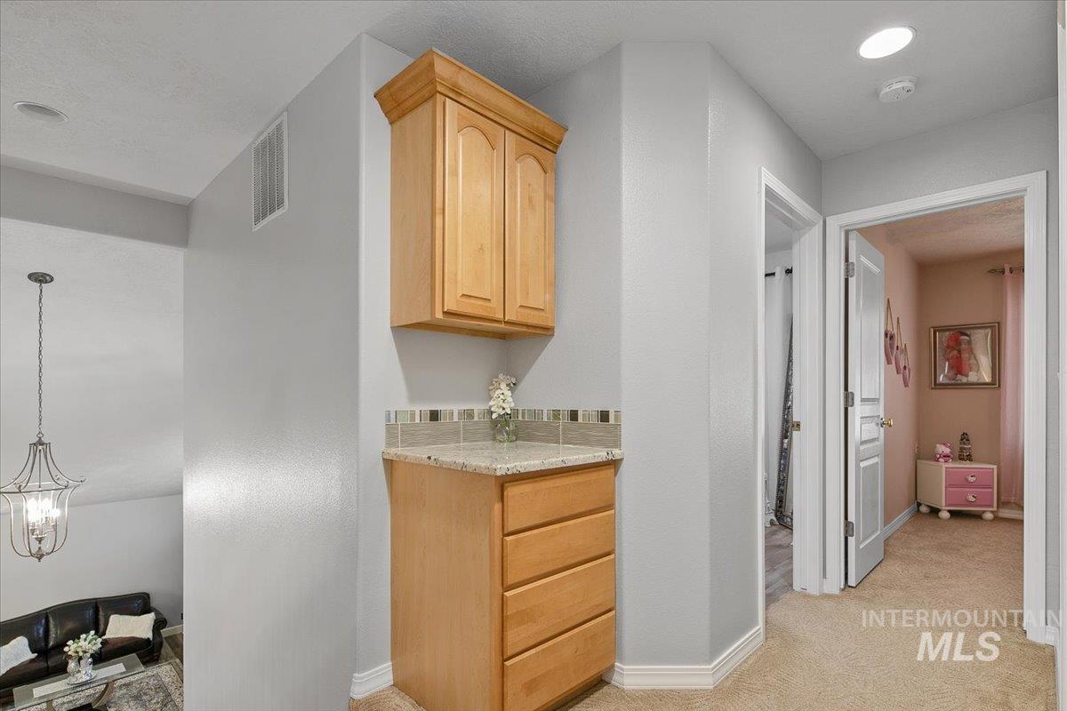 Bar featuring light colored carpet, light brown cabinetry, decorative light fixtures, and light stone counters