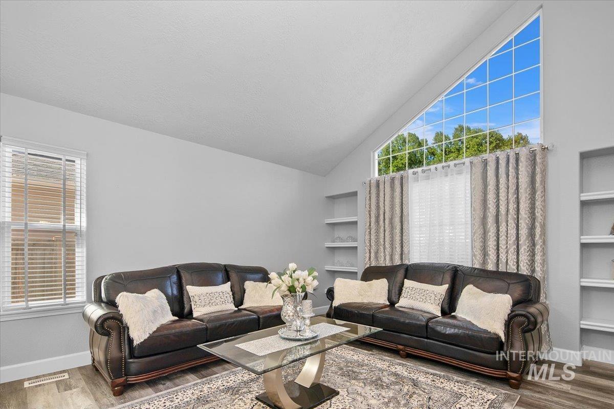 Living room with built in features, wood finished floors, and high vaulted ceiling