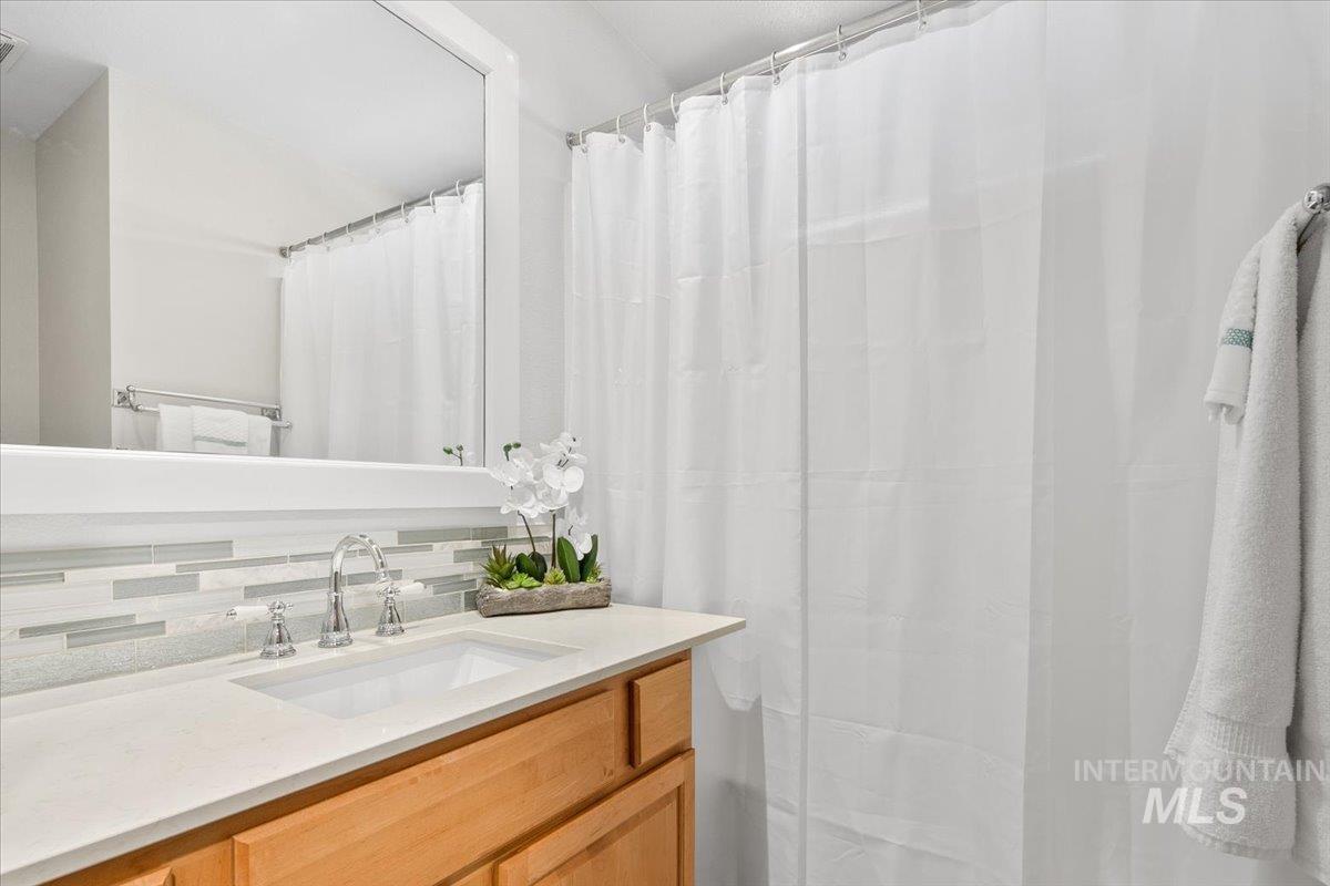 Full bath featuring vanity, decorative backsplash, and a shower with shower curtain