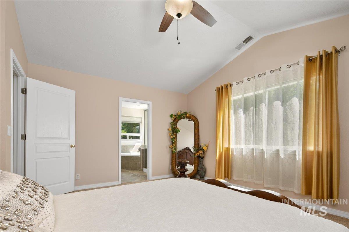 Bedroom featuring lofted ceiling, a ceiling fan, and ensuite bath