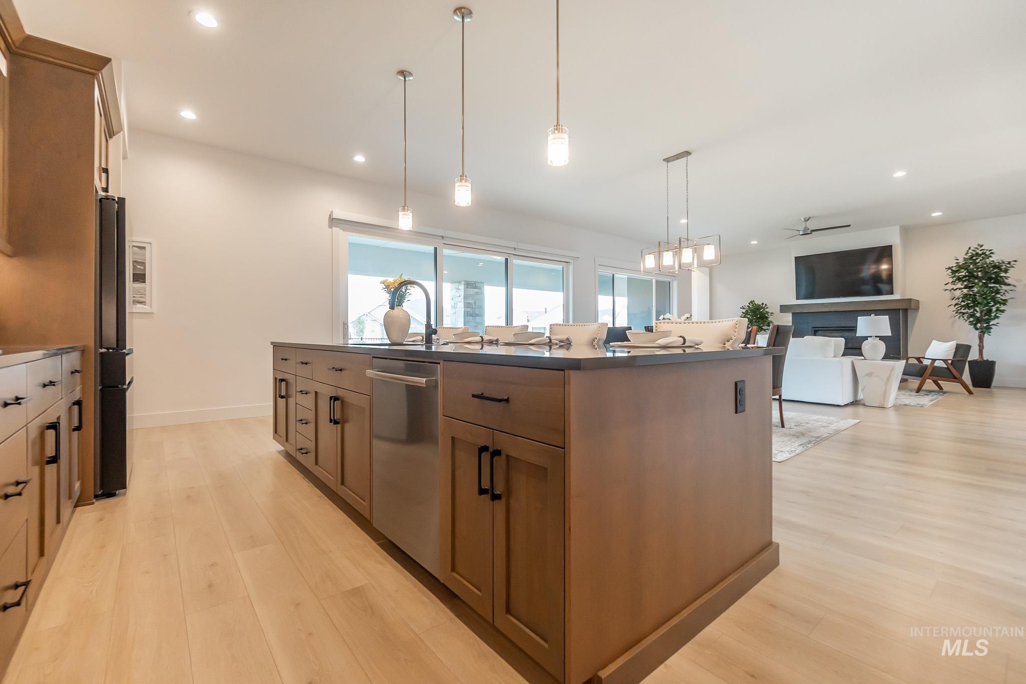 Kitchen featuring dishwasher, dark countertops, light wood finished floors, a center island with sink, and recessed lighting