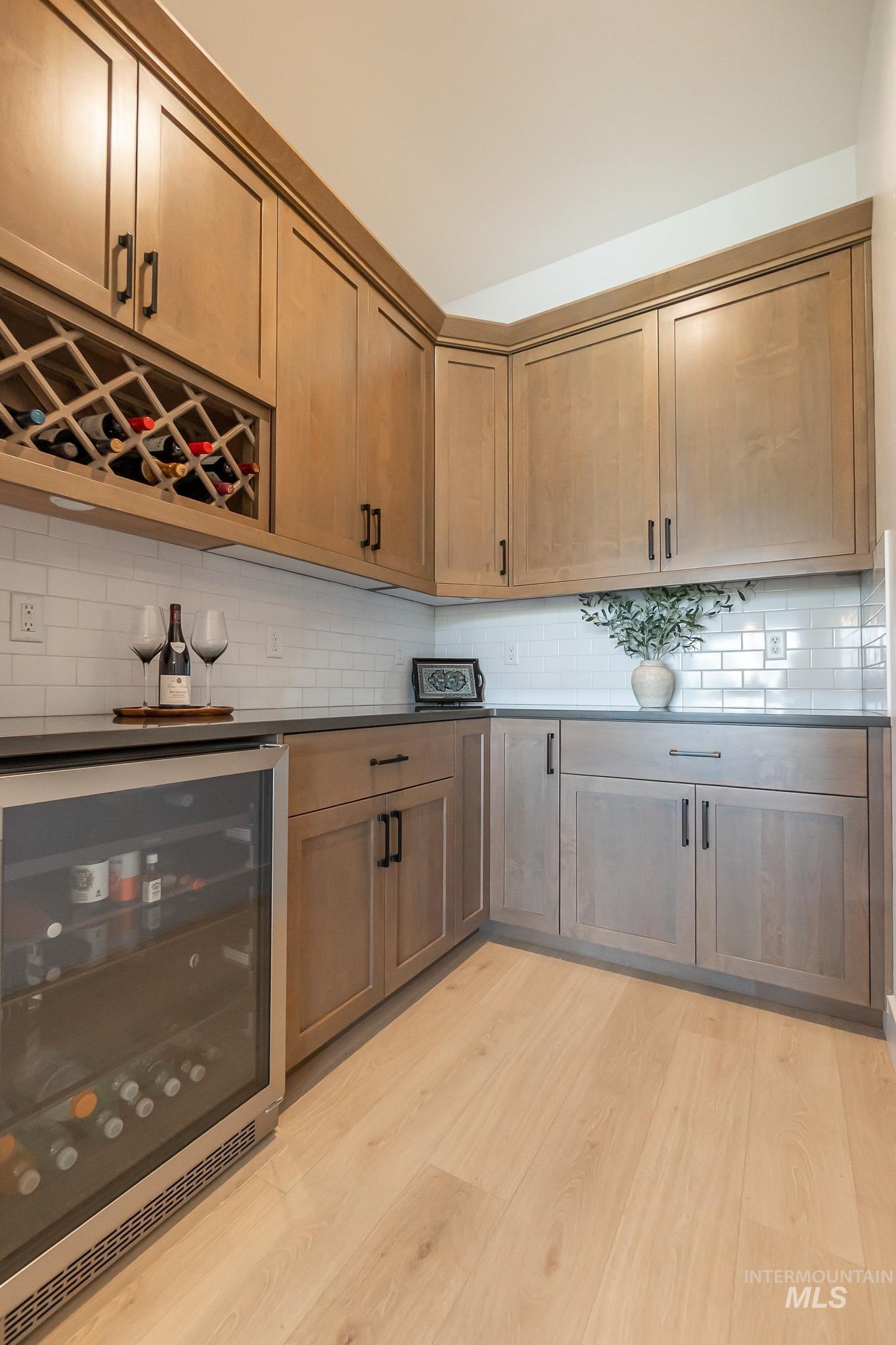 Indoor dry bar featuring wine cooler, light wood-type flooring, and tasteful backsplash