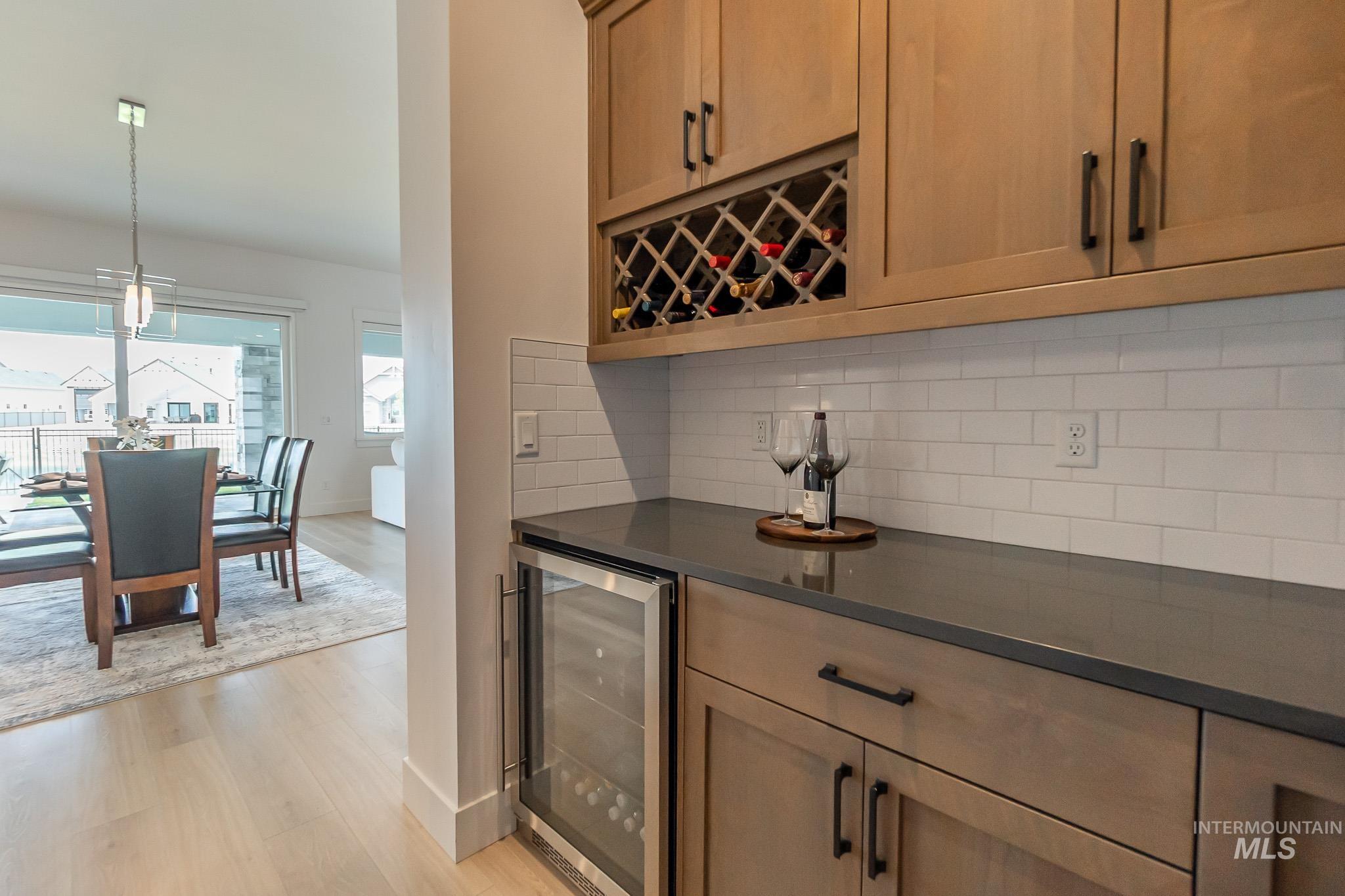 Indoor dry bar with wine cooler, light wood-type flooring, backsplash, hanging light fixtures, and a chandelier