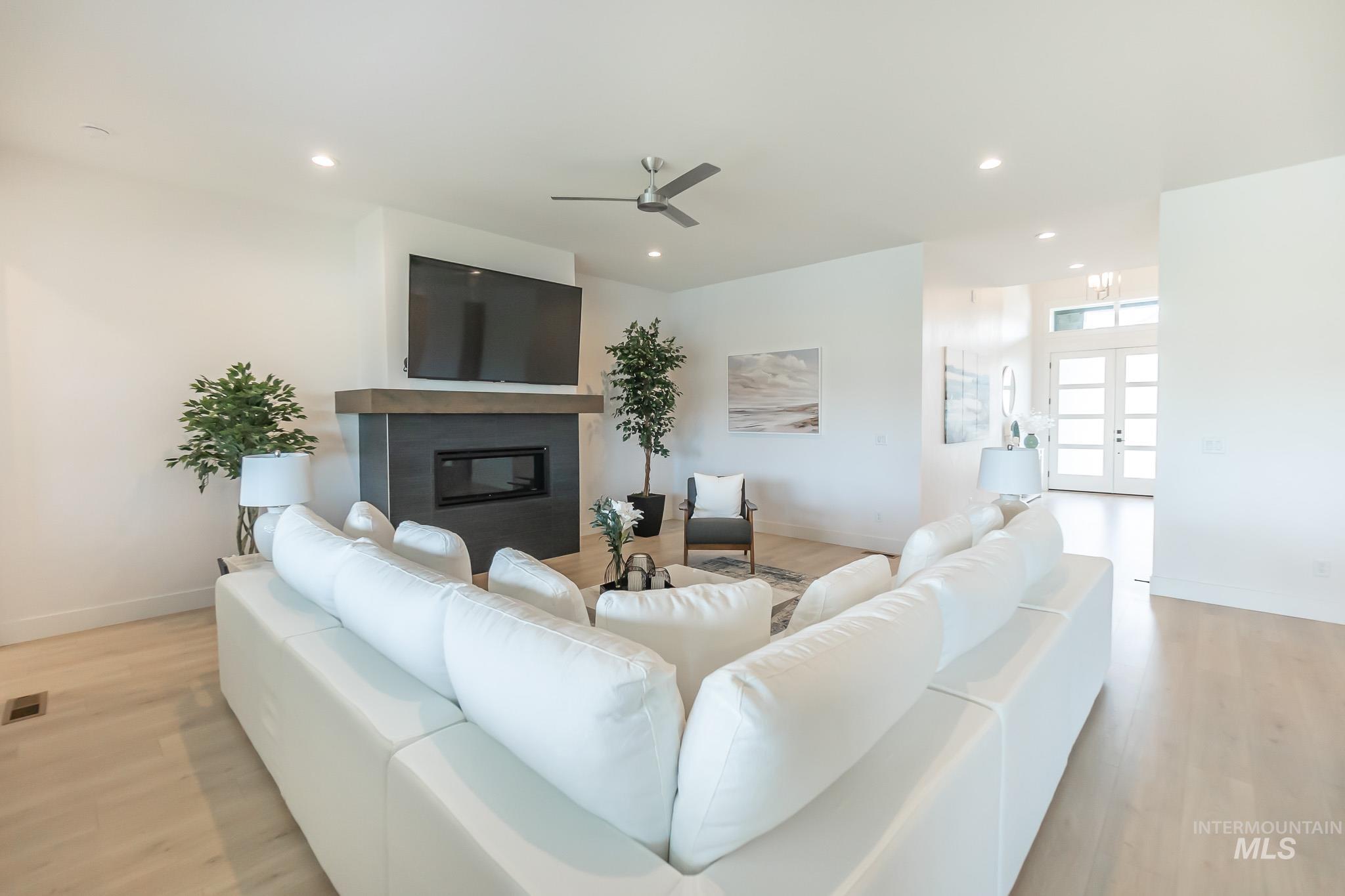 Living room with a glass covered fireplace, light wood finished floors, recessed lighting, french doors, and a ceiling fan