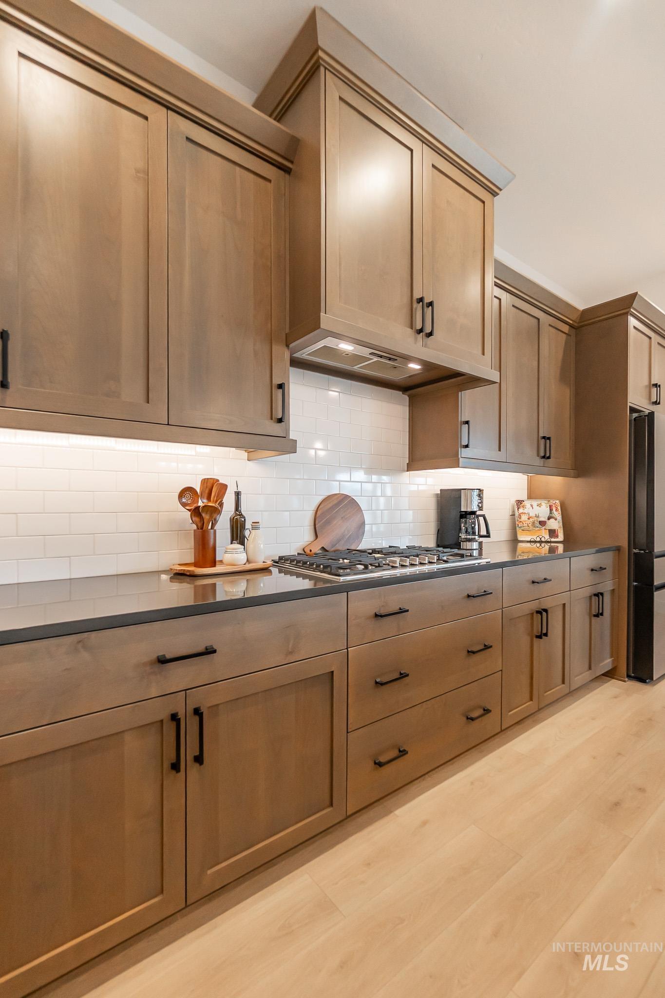 Kitchen featuring dark countertops, freestanding refrigerator, stainless steel gas cooktop, and tasteful backsplash