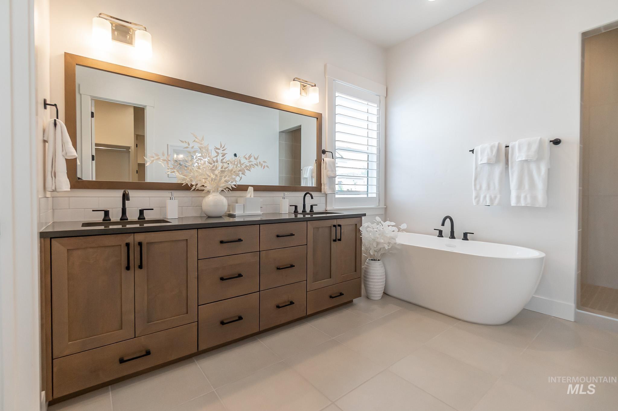Bathroom featuring double vanity, decorative backsplash, a freestanding bath, and tile patterned flooring