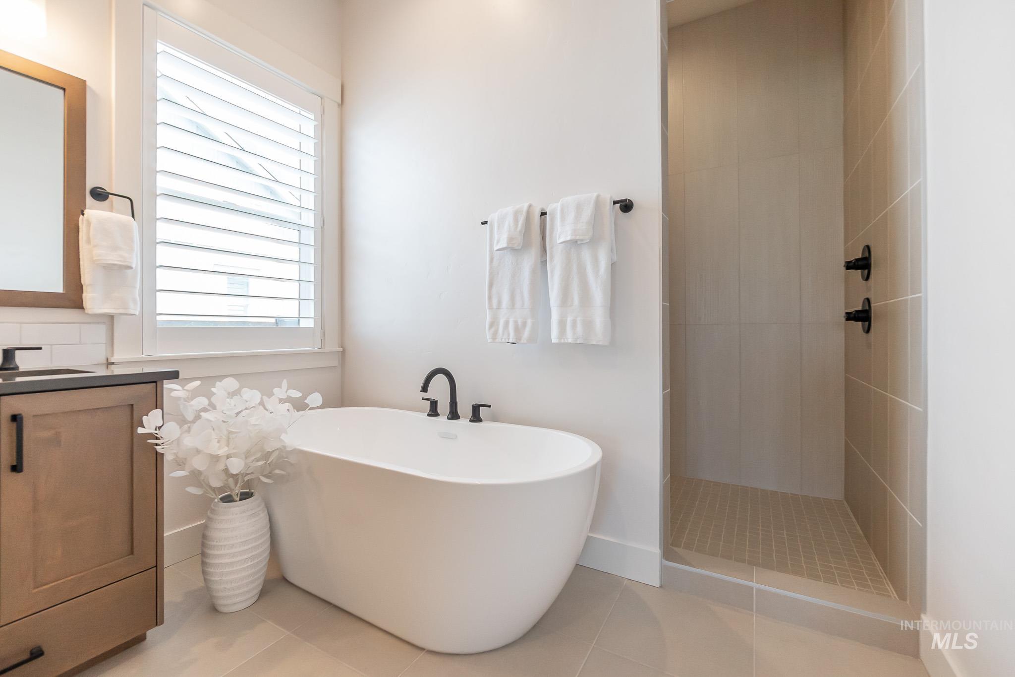 Full bathroom featuring a freestanding bath, tile patterned flooring, a tile shower, and vanity