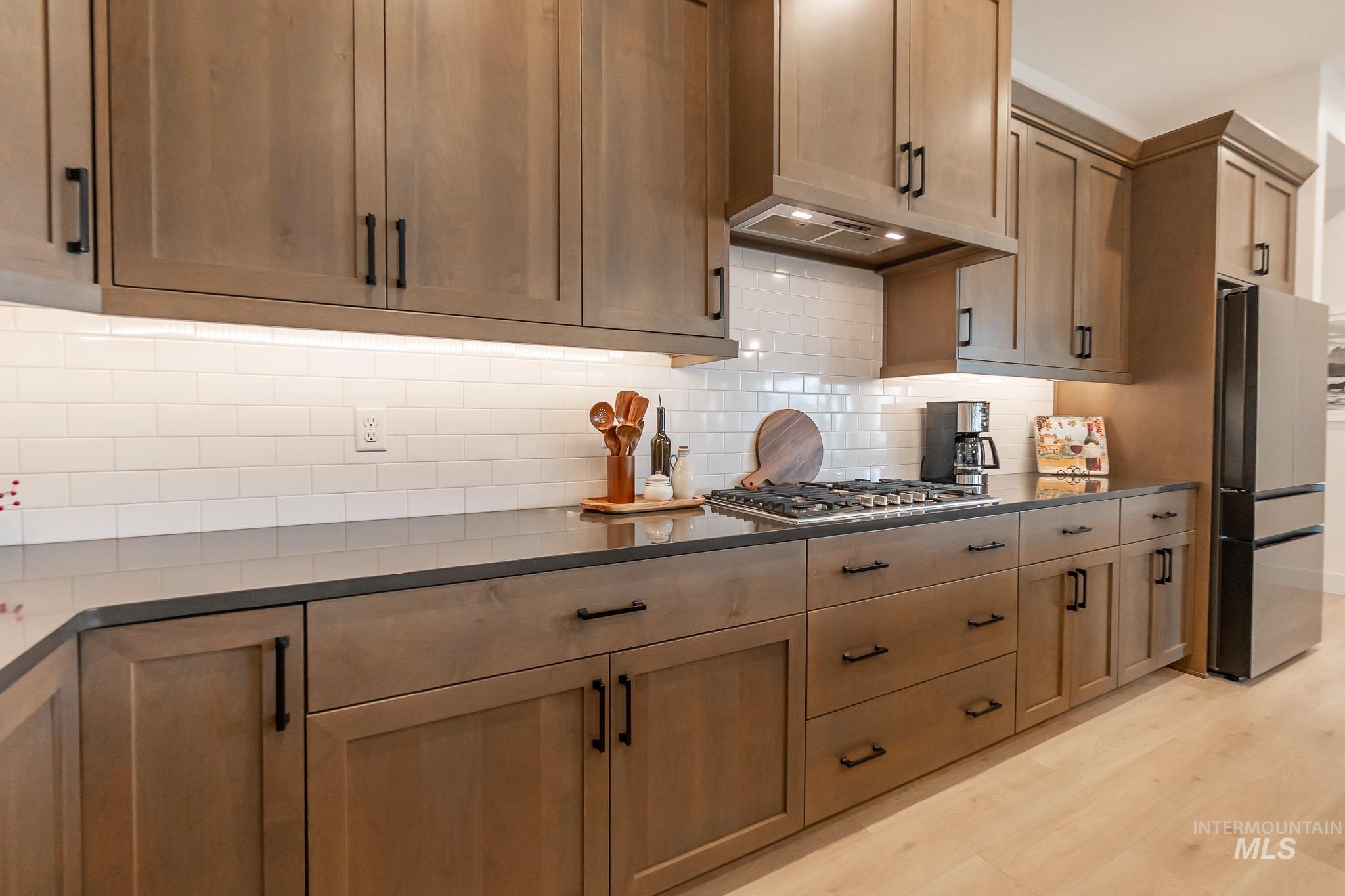 Kitchen featuring dark countertops, appliances with stainless steel finishes, decorative backsplash, light wood-style floors, and exhaust hood