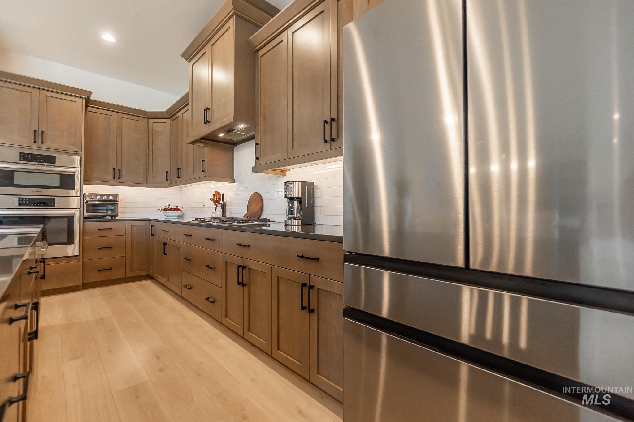 Kitchen featuring stainless steel appliances, backsplash, light wood-type flooring, dark countertops, and recessed lighting