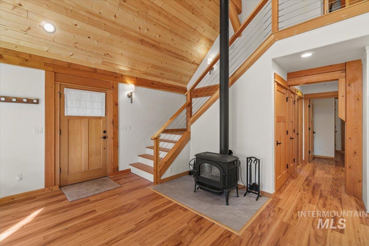 Entryway with a wood stove, recessed lighting, light wood finished floors, wooden ceiling, and stairway