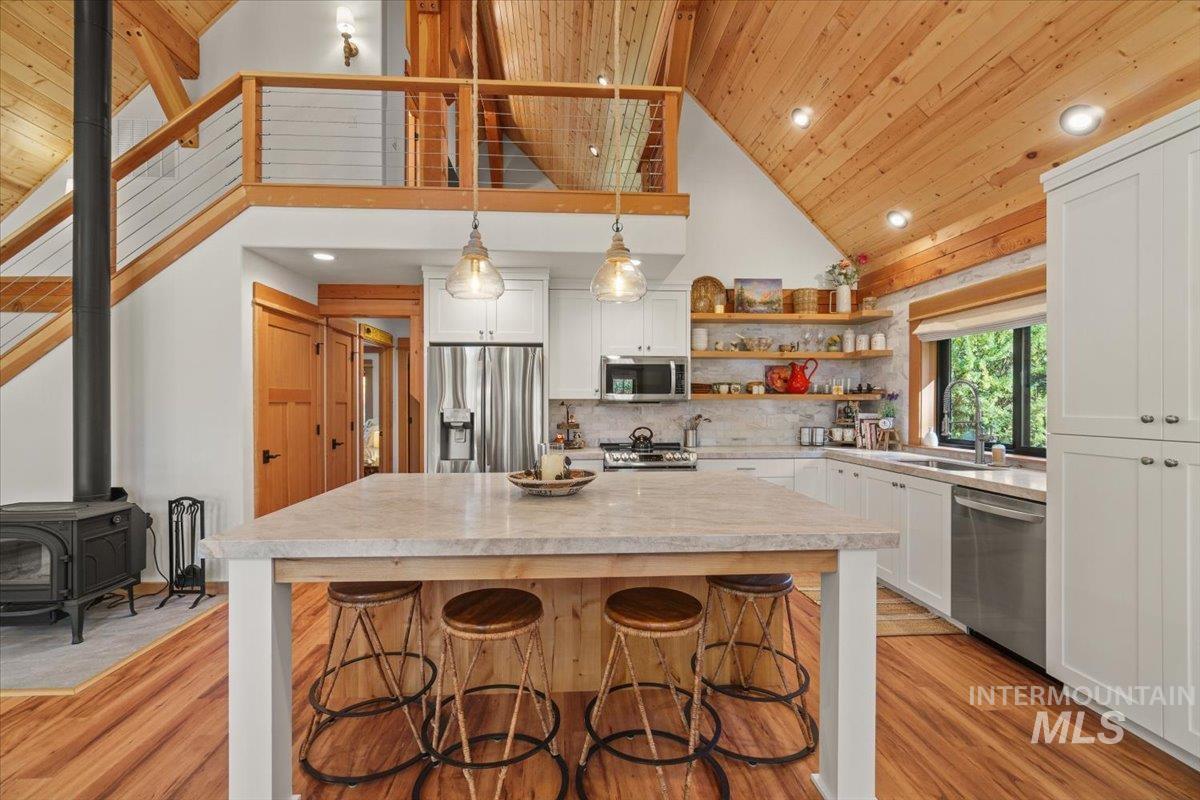 Kitchen with open shelves, decorative backsplash, a wood stove, a breakfast bar area, and decorative light fixtures