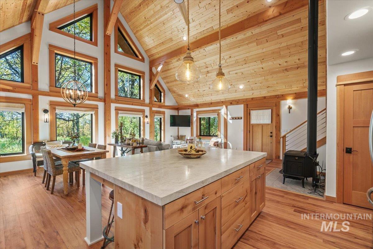 Kitchen with pendant lighting, high vaulted ceiling, a kitchen island, light countertops, and light wood-type flooring
