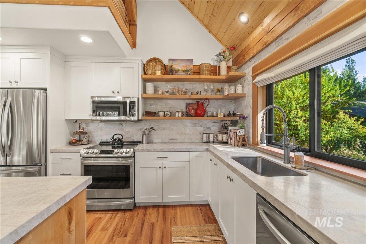 Kitchen with white cabinets, appliances with stainless steel finishes, open shelves, light wood finished floors, and vaulted ceiling