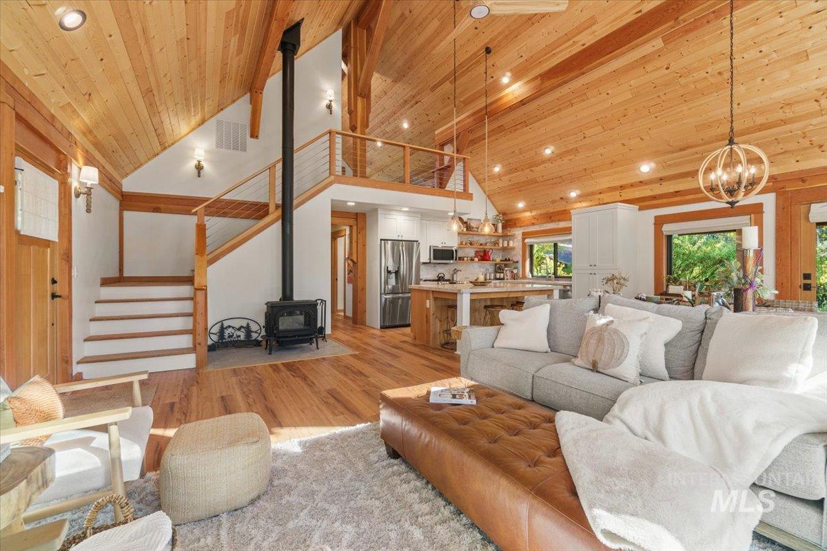 Living room featuring a wood stove, high vaulted ceiling, light wood-style flooring, stairway, and wood ceiling