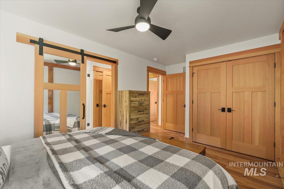 Bedroom featuring wood finished floors, a barn door, ceiling fan, and a closet
