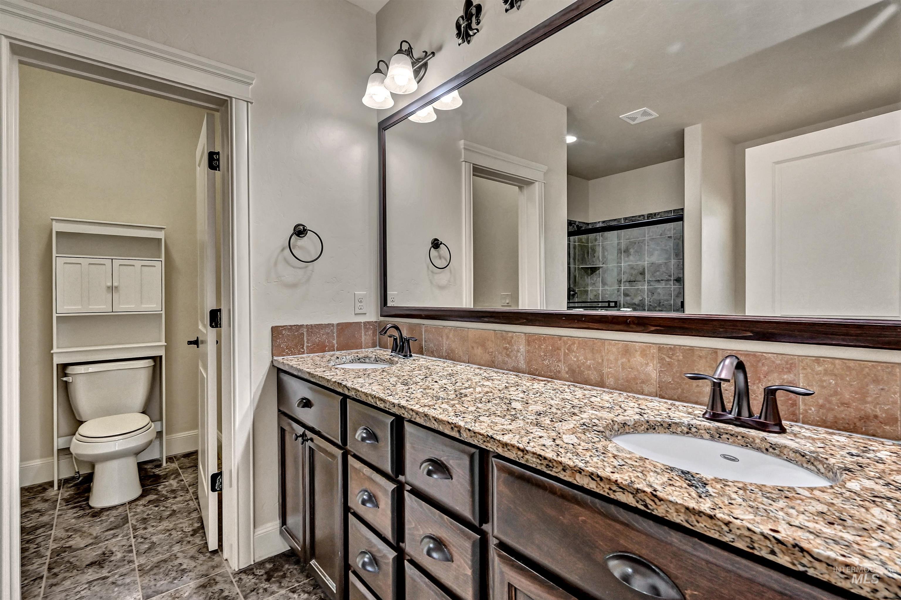 Bathroom featuring double vanity, tiled shower, and dark tile patterned floors