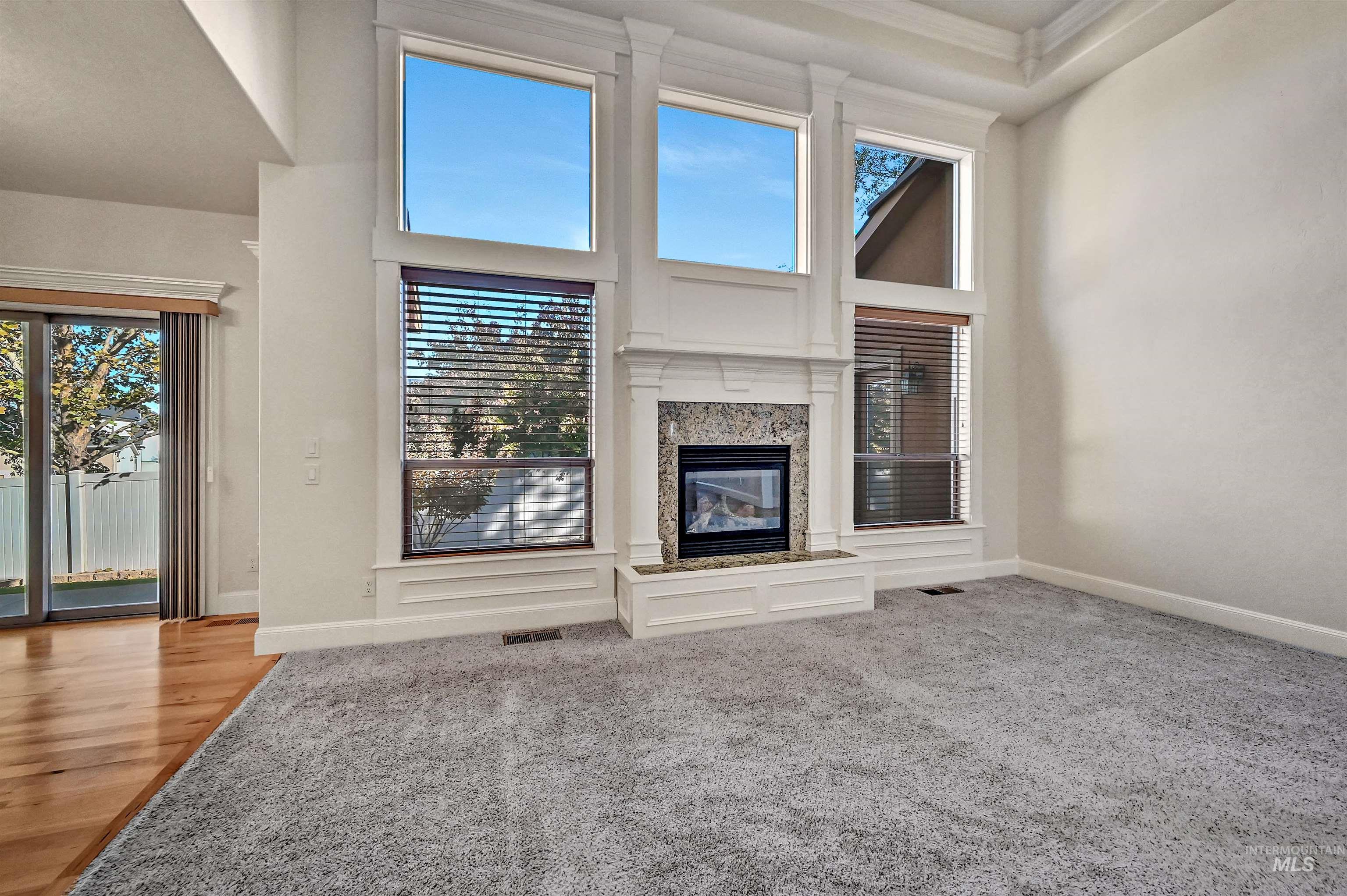 Unfurnished living room featuring a high ceiling, plenty of natural light, a fireplace, and light colored carpet