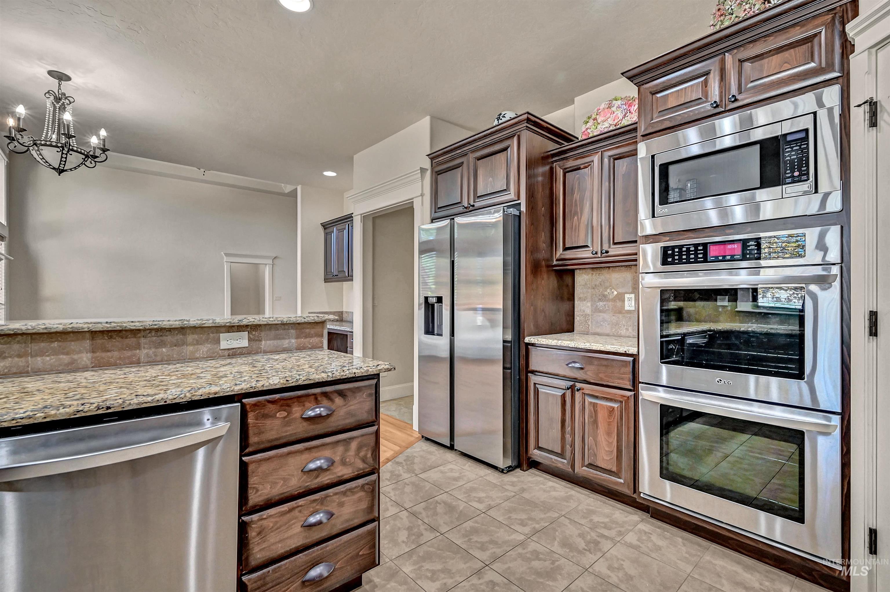 Kitchen featuring stainless steel appliances, light stone countertops, light tile patterned floors, decorative backsplash, and pendant lighting