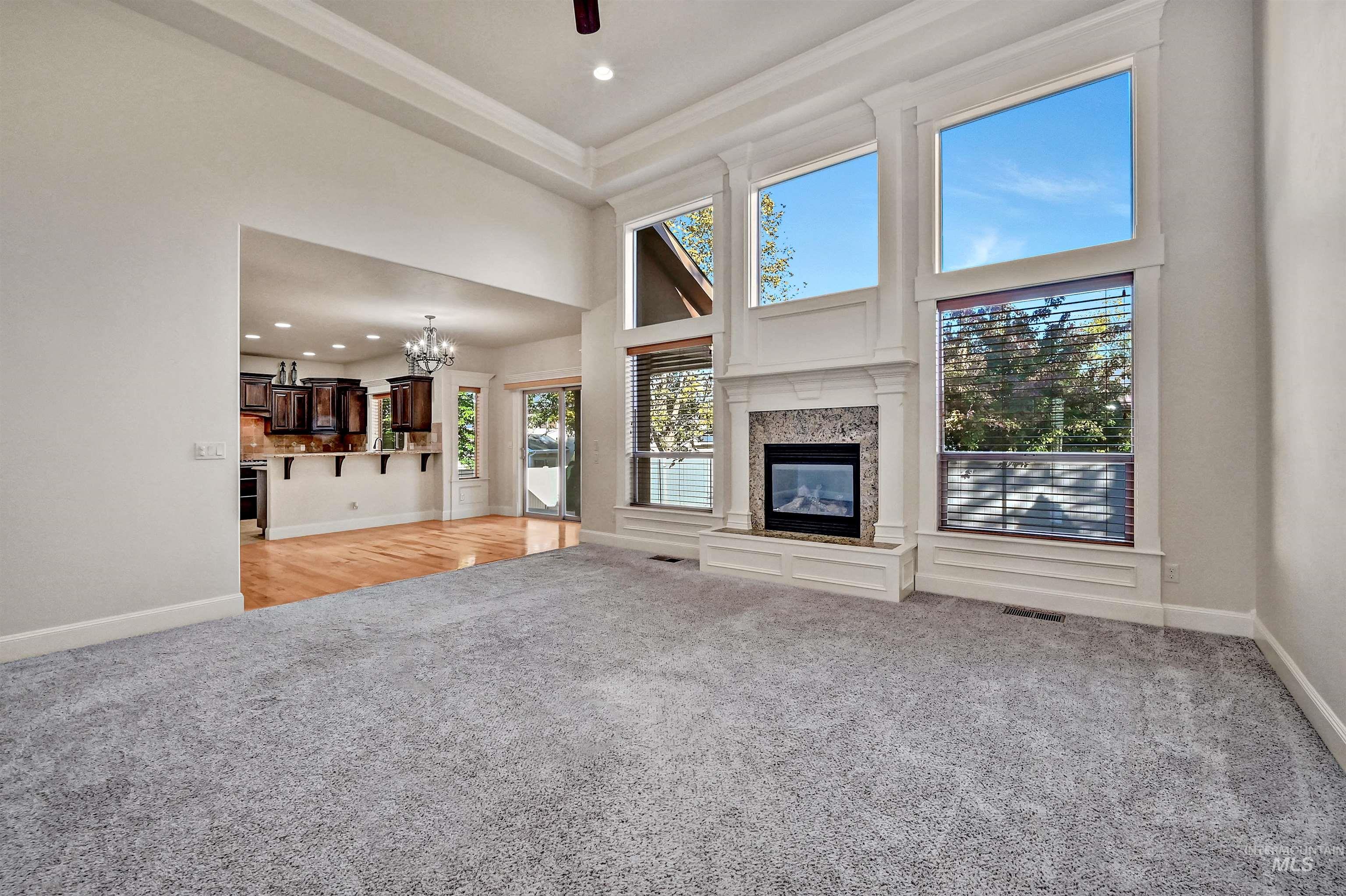 Unfurnished living room with light colored carpet, a towering ceiling, a chandelier, a high end fireplace, and recessed lighting