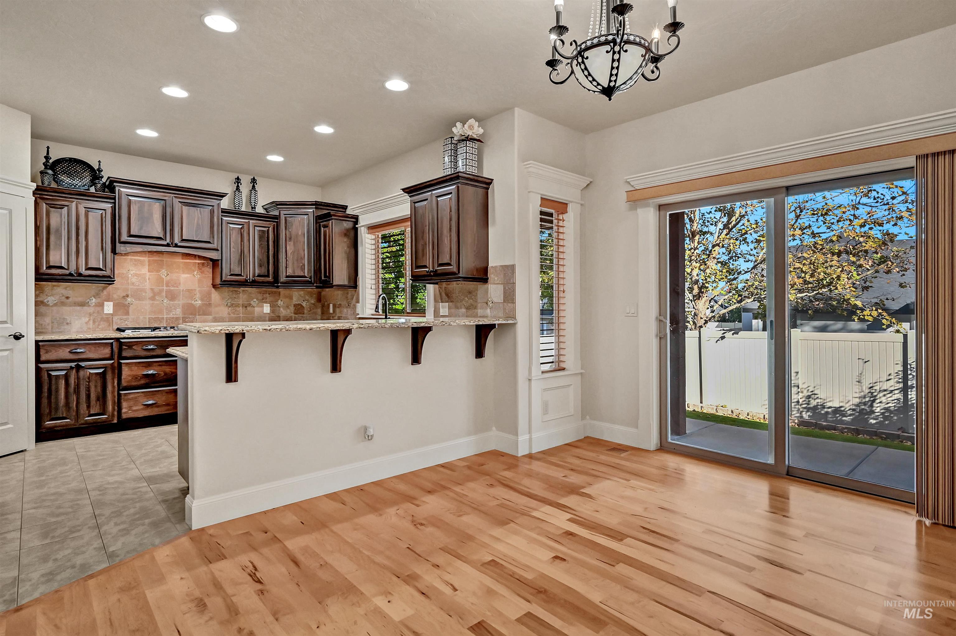 Kitchen with a kitchen breakfast bar, decorative backsplash, dark brown cabinetry, light stone countertops, and recessed lighting